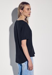 Schwarzes T-Shirt mit kurzen Ärmeln, lässiger Passform und abgerundetem Saum, aus weichem Stoff gefertigt. Kombiniert mit hellblauen Jeans.