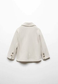Chaqueta texturizada beige con solapa, detalles de costura visibles y cuatro botones en las mangas. Vista trasera que muestra un corte recto y un diseño minimalista.