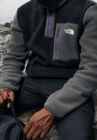 Fleece pullover i sort og grå med en lynlås brystlomme med lilla detaljer. Struktureret stof med en afslappet pasform.