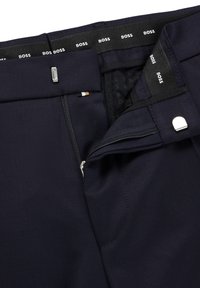 Jūrų mėlynumo kelnės su užtrauktuku ir sagtimi, vidine ženklinimo sistema ir lygaus audinio tekstūra su subtiliomis siuvimo detalėmis.