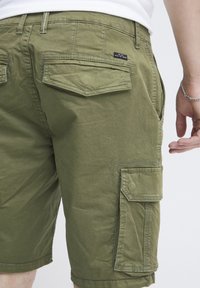 Olivgrüne Cargo-Shorts mit lässiger Passform, mehreren Taschen, gestickten Details und einem Bund mit Gürtelschlaufen.