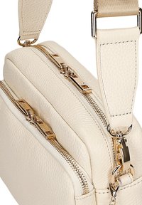 Borsa a tracolla in pelle color crema con due scomparti con zip, dettagli in metallo dorato e finitura testurizzata, dotata di tracolla regolabile.