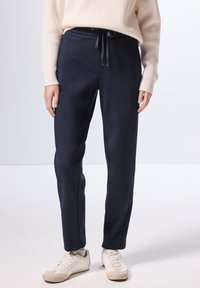 Pantaloni jogger navy in un materiale morbido, con vita regolabile tramite cordoncino, tasche laterali e gambe affusolate, abbinati a sneaker bianche.
