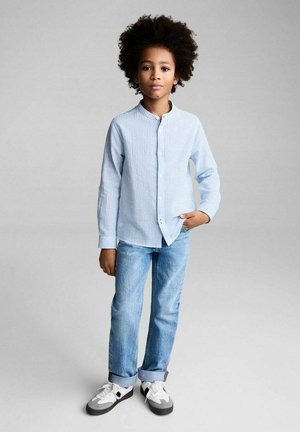 Chemise button-up à manches longues bleu clair avec des rayures verticales, associée à un jean en denim clair et des baskets grises avec des accents noirs.