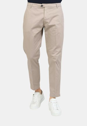 Pantaloni beige con taglio dritto, dotati di passanti per cintura, chiusura con bottone e tasche oblique. Indossati con sneakers bianche.