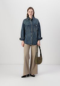 Mørkeblå denimskjorte med to brystlommer og et logo-patch, paret med beige vide bukser og en grønn slingbag. Svarte sko.