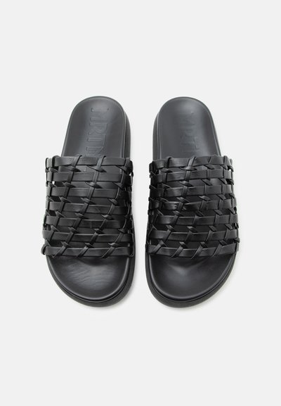 Μαύρα σανδάλια τύπου slip-on με πλεγμένα δερμάτινα λουριά και επίπεδες σόλες, εμφανιζόμενα από πάνω σε λευκό φόντο.