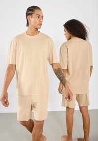 Beige pamut póló és rövidnadrág szett, laza illeszkedéssel. Sim felület, rövid ujjakkal, látható minták vagy fém kiegészítők nélkül.