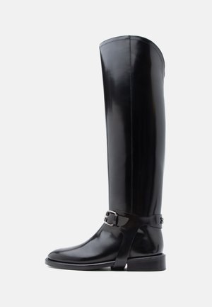 Mustad põlvikuni saabuvad saapad läikivast materjalist, millel on lai sääreosa, pandlaga rihm ja madal konts. Sile tekstuur ja minimaalne detailirohkus.