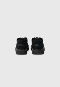 Scarpe in suede nero con suola piatta, dotate di un logo sul tallone, cuciture a contrasto e un design semplice e arrotondato.