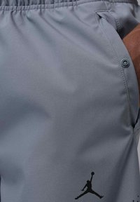 Szare sportowe spodenki wykonane z gładkiej tkaniny. Posiadają boczne kieszenie, elastyczny pas i wyraźnie widoczne czarne logo.