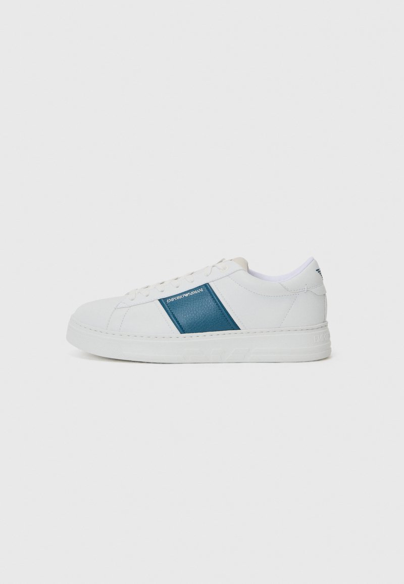 Vita sneaker med blå läderpanel, rund tå, platt gummisula och snörning. Har logotyp på sidan och texturdetalj på panelen.