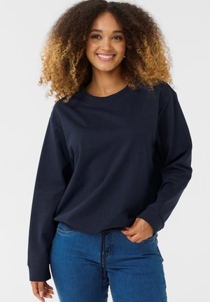 Navy blue sweatshirt with long sleeves and a round neck, paired with blue jeans. Features a drawstring at the waist. Smooth fabric texture.
