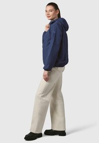 Tamsiai mėlyna gobtuvu su elastinėmis rankogaliais, derinama su kreminėmis plačiomis kelnėmis ir juodais batais su storu padu. Lygios audinio tekstūros.