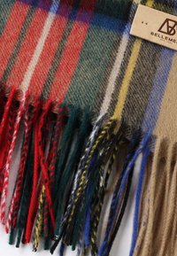 Sciarpa multicolore con motivo a quadri caratterizzata da strisce rosse, verdi, gialle e blu. Ha bordi frangiati e un tag in pelle.