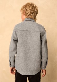 Veste-chemise grise à motif chevrons en tissu texturé, avec un col et des manches longues, dotée de poignets à boutons.