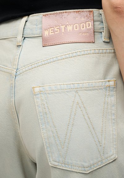 Πίσω τσέπη ανοιχτό μπλε τζιν με ραμμένο σχέδιο "W" και καφέ δερμάτινη ετικέτα στη μέση με την επιγραφή "WESTWOOD JEANS".