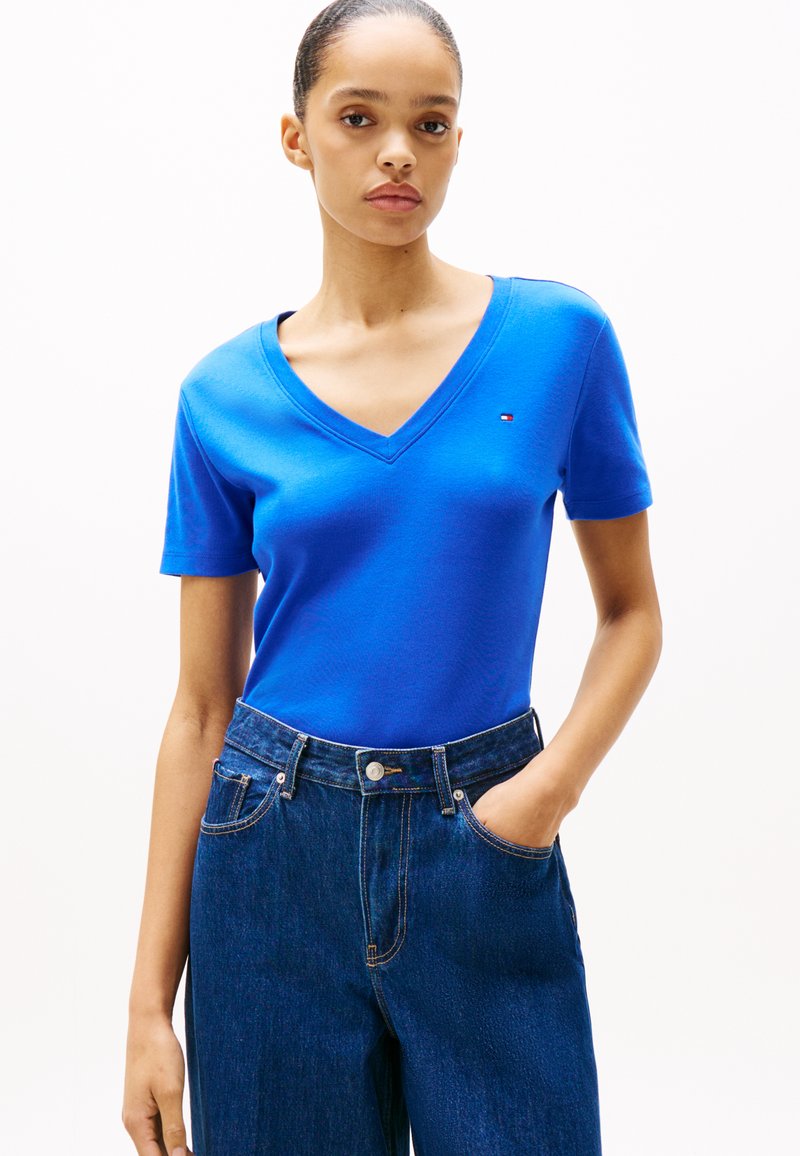 Blauwe V-hals T-shirt van een gladde stof, met korte mouwen en een kleine logo-accent. Gecombineerd met high-waisted spijkerbroeken.