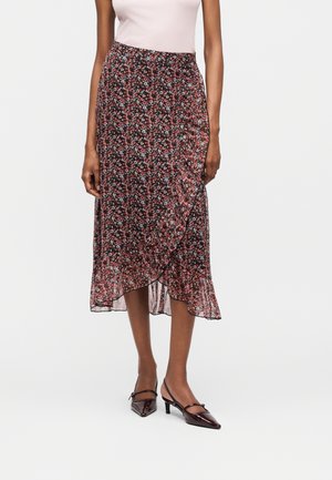 Γυναίκα με μαύρη μεσαία φούστα με μικρά κόκκινα και λευκά λουλούδια, σε συνδυασμό με ανοιχτό ροζ τοπ και σκούρα μυτερά τακούνια.