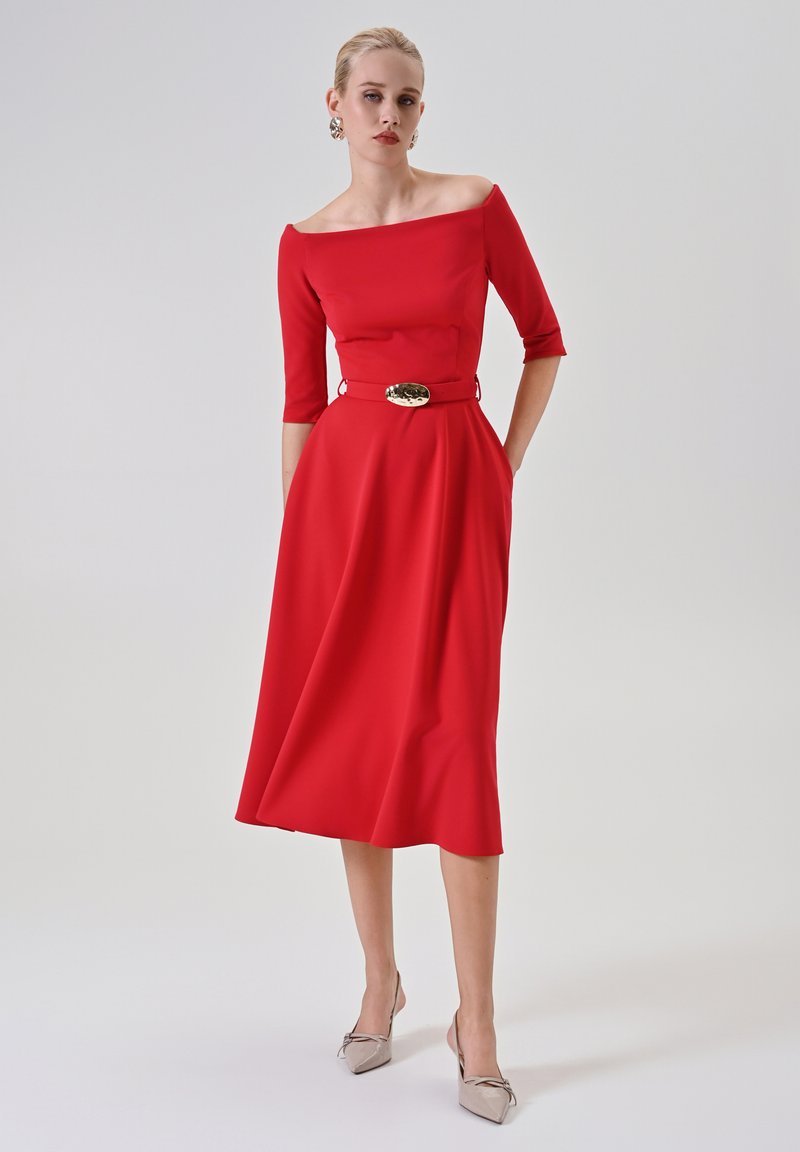 Rotes Midi-Kleid mit schulterfreiem Ausschnitt, drei Viertel-Ärmeln und taillierter Passform. Mit einem goldenen Gürtelakzent und glatter Textur.