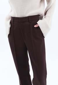 Bruine op maat gemaakte broek van gestructureerde stof met een slim fit, voorzien van zijzakken en een vlakke voorkant, gedragen met een crèmekleurige oversized trui.