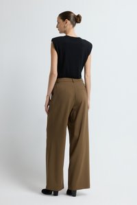 Zwart mouwloos topje gecombineerd met hooggetailleerde, wijde bruine broek. Glad stof met een subtiele glans. Hakken zorgen voor extra lengte.