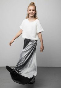 Biały dzianinowy top z krótkim rękawem w połączeniu z długą, zwiewną, plisowaną szarą spódnicą przechodzącą w czerń przy obrzeżu, noszony z czarnymi butami.