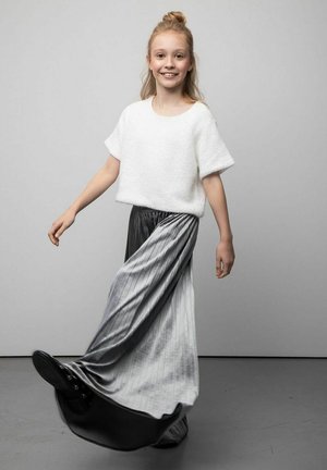 Biały dzianinowy top z krótkim rękawem w połączeniu z długą, zwiewną, plisowaną szarą spódnicą przechodzącą w czerń przy obrzeżu, noszony z czarnymi butami.