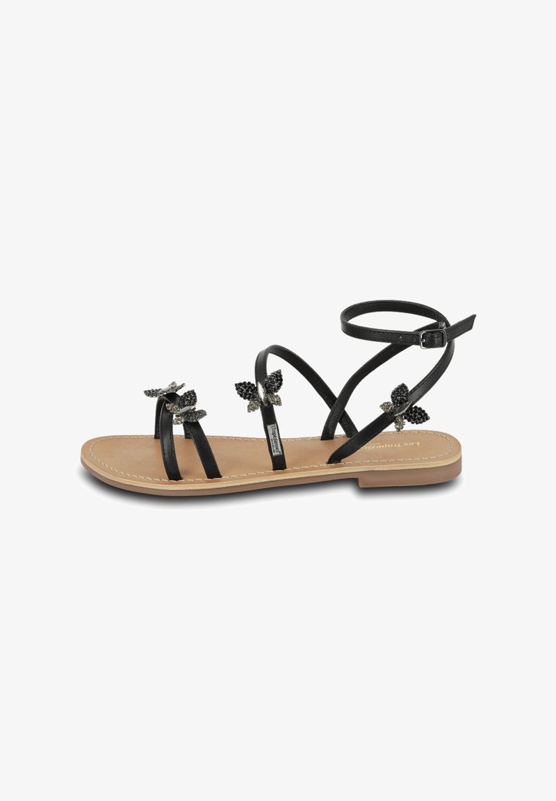 Sandalias planas negras con tres correas delgadas y una correara en el tobillo. Decoradas con adornos de mariposas negras. Plantilla de color marrón suave. Diseño sencillo.