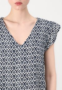 Mörkblå och vit mönstrad topp med V-ringning, korta samlade ärmar och strukturerad tyg med geometrisk design.