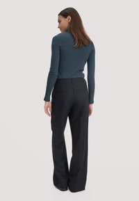 Langsleeve teal top en zwarte pantalon op maat. Top heeft een ronde halslijn; de broek heeft een vlakke voorkant met zakken en een rechte pijp.