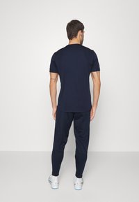 Marine T-Shirt mit kurzen Ärmeln und Rundhalsausschnitt, kombiniert mit passenden Sporthosen. Beide Teile haben eine glatte Textur und eine taillierte Passform.