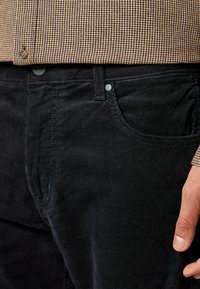 Zwarte corduroy broek met verticale ribbels, voorzien van een standaard vijf-pocket ontwerp en metalen knoopaccenten bij de tailleband.