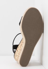 Black wedge sandal with cork platform and textured sole. Features adjustable strap and branded label on the footbed. Made in China.