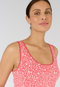 Top senza maniche a fantasia floreale in rosa con fiori bianchi, caratterizzato da un collo a giro e bordi scallop. Realizzato in tessuto leggero.
