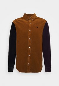 Camisa de pana con parte frontal de color marrón anaranjado, mangas de color púrpura oscuro y negro, cuello canadiense y botones blancos, con un pequeño logo en el pecho.