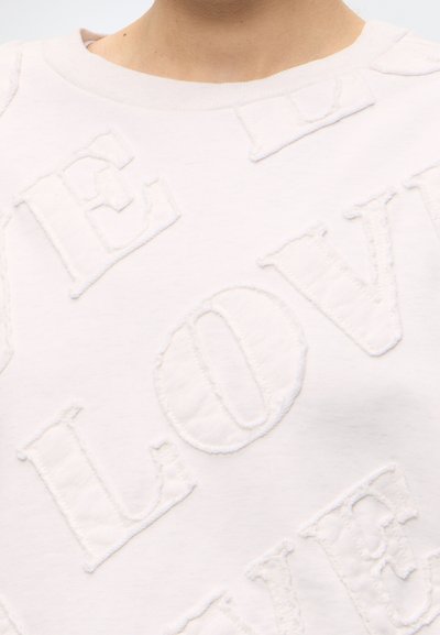 Gros plan d'un sweat-shirt blanc avec des lettres en relief et texturées formant le mot « LOVE » qui se chevauchent.
