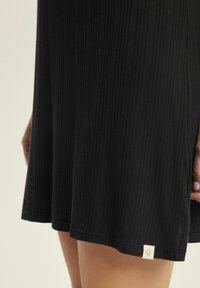 Czarna sukienka z prążkowaną teksturą i lekkim rozkloszowaniem. Zawiera małą metkę przy dolnym brzegu z logo. Gładkie wykończenie materiału.