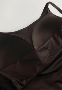 Primer plano de un sujetador acolchado marrón oscuro con bordes cosidos y tirantes ajustables sobre un fondo claro.