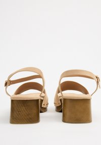 Sandalias de plataforma en color nude con un acabado de ante suave, tiras en el tobillo y tacón de bloque de madera, con tachuelas doradas decorativas en los laterales.