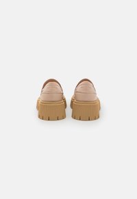 Scarpe in pelle beige con una suola spessa, scanalata e color tan, e un retro arrotondato. Dettagli cuciti e nome del marchio impresso sui lati.