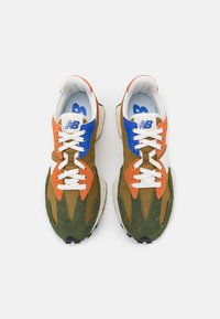 Pár vícebarevných tenisek New Balance s akcenty v zelené, oranžové, modré a bílé barvě, z pohledu shora na bílém pozadí.
