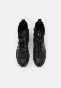 Botines negros de piel suave con punta redonda, diseño de cordones, ojales plateados y cremallera lateral para facilitar su uso.