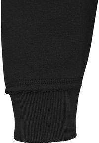 Jambe de pantalon en tissu noir avec un poignet côtelé élastique et une couture visible au-dessus du poignet, montrant une texture lisse et des coutures serrées.