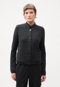 Cárdigan texturizado en gris oscuro con cuello mao, cierre frontal de seis botones y dos bolsillos frontales. Lleva puesto sobre pantalones a rayas.