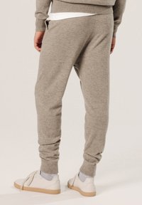 Helle graue, gestrickte Jogginghosen mit gerippten Bündchen und Seitentaschen, kombiniert mit weißen Sneakern und grauen Knöchelsocken. Glatte Textur und entspannter Schnitt.