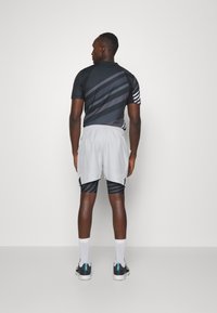 Camiseta deportiva negra y gris con franjas diagonales, combinada con pantalones cortos gris claro. Cuenta con mangas cortas y bolsillos laterales.