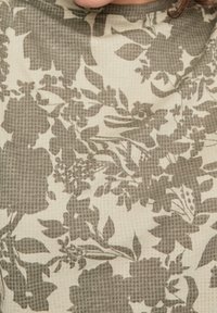Tkanina w kwiatowy wzór w stonowanych odcieniach oliwkowej zieleni i kremu, o teksturowanej powierzchni oraz szczegółowych wzorach kwiatów i liści.