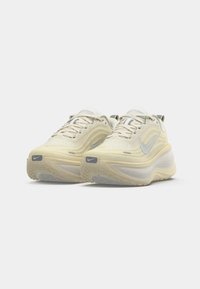 Μπεζ αθλητικά παπούτσια με υφασμάτινη επάνω επιφάνεια με υφή, εξέχον λογότυπο της Nike σε α�σημί χρώμα, επενδεδυμένος λαιμός και χοντρή καουτσούκ σόλα με μοτίβο.