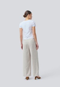 T-shirt bianco a maniche corte abbinato a pantaloni larghi beige chiaro. I pantaloni presentano un tessuto testurizzato e tasche laterali, abbinati a tacchi marroni.